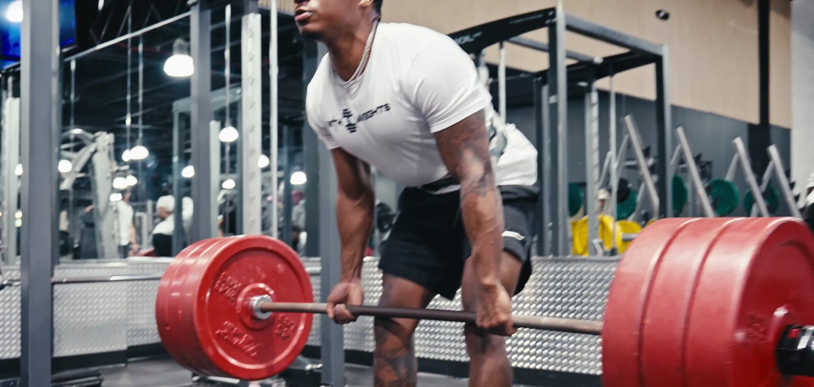 Damone Jackson pulling a heavy barbell deadlift with red plates in the gym